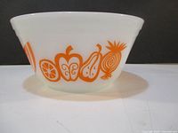 Side view of vintage white glass mixing bowl showing orange fruit designs including apple, pear, and other fruits.