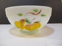 Side front view of white opaque milk glass bowl with painted yellow peaches and green leaves, showing design details and condition.