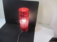 Front-side angle showing the lit red rattan woven cylindrical lamp with visible black base and power cord.
