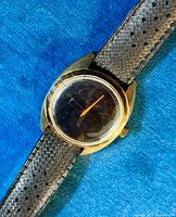 Top-down view of watch on blue background showing black dial, orange-red hands and cushion case