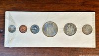 Full view of the six Canadian coins from 1964 sealed in original packaging showing silver dollar, 50 cent, 25 cent, 10 cent, nickel 5 cent and bronze penny coins.