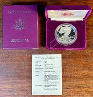 Purple velvet box with American Eagle silver bullion coin, COA card on wooden surface.