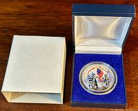 Coin in presentation box next to outer white sleeve on wooden surface