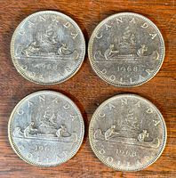 Four 1968 Canadian silver dollar coins arranged on wooden surface.