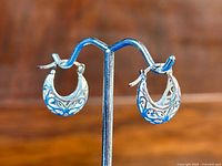 Pair of crescent-shaped hoop earrings displayed on stand, showcasing intricate engraved floral pattern across both earrings.