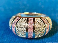 Close-up front view of the sterling silver ring showing alternating rows of pink square-cut stones and clear round stones in pave setting against a blue background.