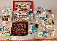 Wide view of dollhouse miniatures with carpet, various packaged miniatures and small signs, some loose items laid out.