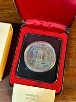 Close-up of the reverse side of the silver dollar depicting the Canadian Senate throne within its plastic capsule and red velvet presentation case.
