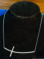 Front view of the necklace displayed on black velvet bust showing the full chain and sideways cross pendant with rhinestones.