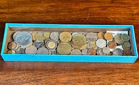 Top-down view of tray filled with assorted old coins including international varieties, showing various sizes and metal colors.