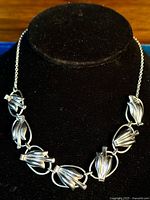 Front view of the entire silver necklace displayed on a black velvet stand showing the linked floral-shaped segments and chain.