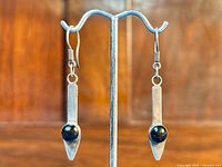 Front view of the pair of sterling silver dangle earrings showing the narrow rectangular shape and black onyx stone on each earring.