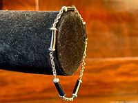 Side angle view showing the onyx pillars spaced along the sterling silver chain bracelet on a black velvet stand.