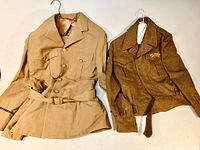 Two wool uniform jackets laid flat: left tan RCAF style jacket with belt, right brown cadet jacket with patch