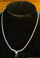 Full view of the silver Celtic necklace on a black display stand showing its chain length and the central pendant with a blue stone.