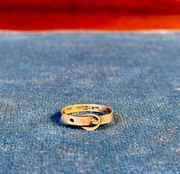 Single vintage sterling silver ring styled as a belt with buckle on the band, shown on a blue background