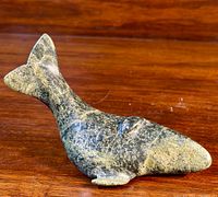Soapstone whale carving showing profile and tail fin detail on a wood surface.