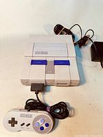 Front view of the Super Nintendo Entertainment System console with the controller plugged in, showing Power, Reset, and Eject buttons and the included cords.
