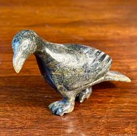 Front angle view of the dark soapstone bird carving showing detailed head and feet on a wooden surface.