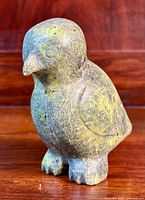 Front view of the soapstone puffin carving showing bird facial features, rounded body, and feet details, set against a wooden background.