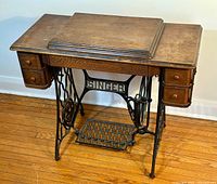 Full view of the antique Singer treadle sewing machine with wood stand and drawers, showing the cast iron treadle base and wooden top.
