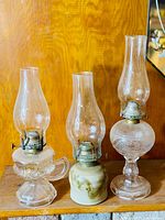 Photo showing three vintage coal oil finger lamps together, highlighting varied base materials and intact chimneys.