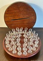 Photo showing entire communion cup set with 35 pressed glass cups arranged in round wooden carrier box with lid against wall background.