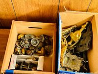Overview photo showing multiple glass, brass, and wooden doorknobs together with brass hardware parts and a door knocker in two open boxes.