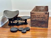 Overall view of the antique cast-iron balance scale with the four cast-iron weights and original wooden storage box, showing condition and relative sizes.