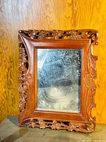 Full front view of antique carved wood framed mirror showing ornate floral and leaf carved edges and aged mirror surface.