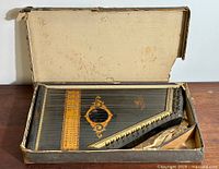Antique Zither auto harp in original box showing full instrument body with decorative gold leaf designs and strings.