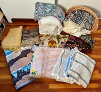Collection of 11 blankets and throws on wooden floor showing a variety of textures, colors, and patterns.