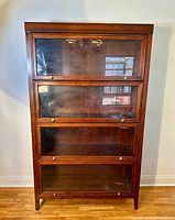 Front-facing view of the full bookcase showing four stacked glass-drop doors and overall finish