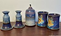 Five pottery pieces displayed: two candlesticks, one oil lamp base, and two mugs.