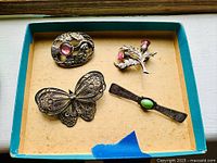 Overview of all five brooches in a cardboard tray showing different designs and gemstone accents