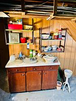 Wide shot of wooden cabinet with marble top, shelves with dishes and kitchenware, and other items on and above cabinet.