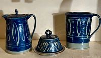 Set showing covered butter dish with lid, pitcher, and karafe side by side with dark blue glaze and white patterns.