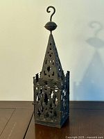 Front side view of the ornate metal lantern with hook on top and intricate cut-outs.