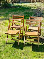 Four wooden folding slat chairs set up outdoors on grass showing overall condition and design.