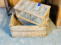 Photo showing the small wooden seedling greenhouse on top of the rustic wooden crate. The greenhouse has transparent panels and a hinged lid.