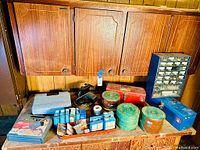 Wide shot of wooden cupboard with three doors. Front surface used as workspace holding toolboxes, spools of jute, and hardware boxes.