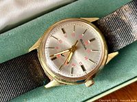 Close-up of men’s watch face showing Bulova logo, silver dial, red 24-hour numerals and whale symbol at 6 o’clock.