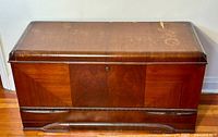Front view of the cedar chest showing wood veneer pattern, decorative carving, and keyhole.