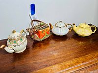 Four vintage teapots placed on wooden surface showing all items in the lot.