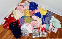 Full view of assorted vintage children's clothing spread on the floor showing many types, styles and colors including dresses, sweaters, bonnets, and mittens