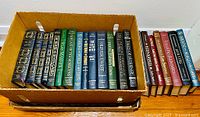 Photo showing 18 hardcover books in a box and stacked beside it, with decorative gilded spines. Titles visible include classics like 'The Call of the Wild', 'Oliver Twist', and 'The Last of the Mohicans'.