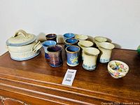 Overview of all pottery items including covered casserole, tumblers, cups, and small bowl on wooden surface