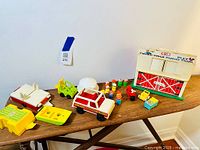 Overview of Fisher Price Farm Barn with vehicles and Little People figures displayed on wooden table.