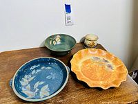 Four signed handcrafted studio pottery pieces including platters, bowl, and small lidded jar on wooden surface.