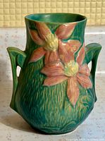 Front view of Roseville Clematis pottery vase showing pink clematis flowers, two handles, and textured green background.
